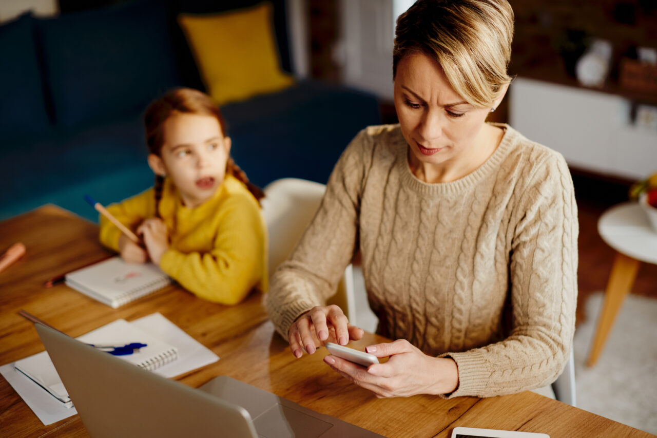 Mid adult mother using smart phone while working at home.